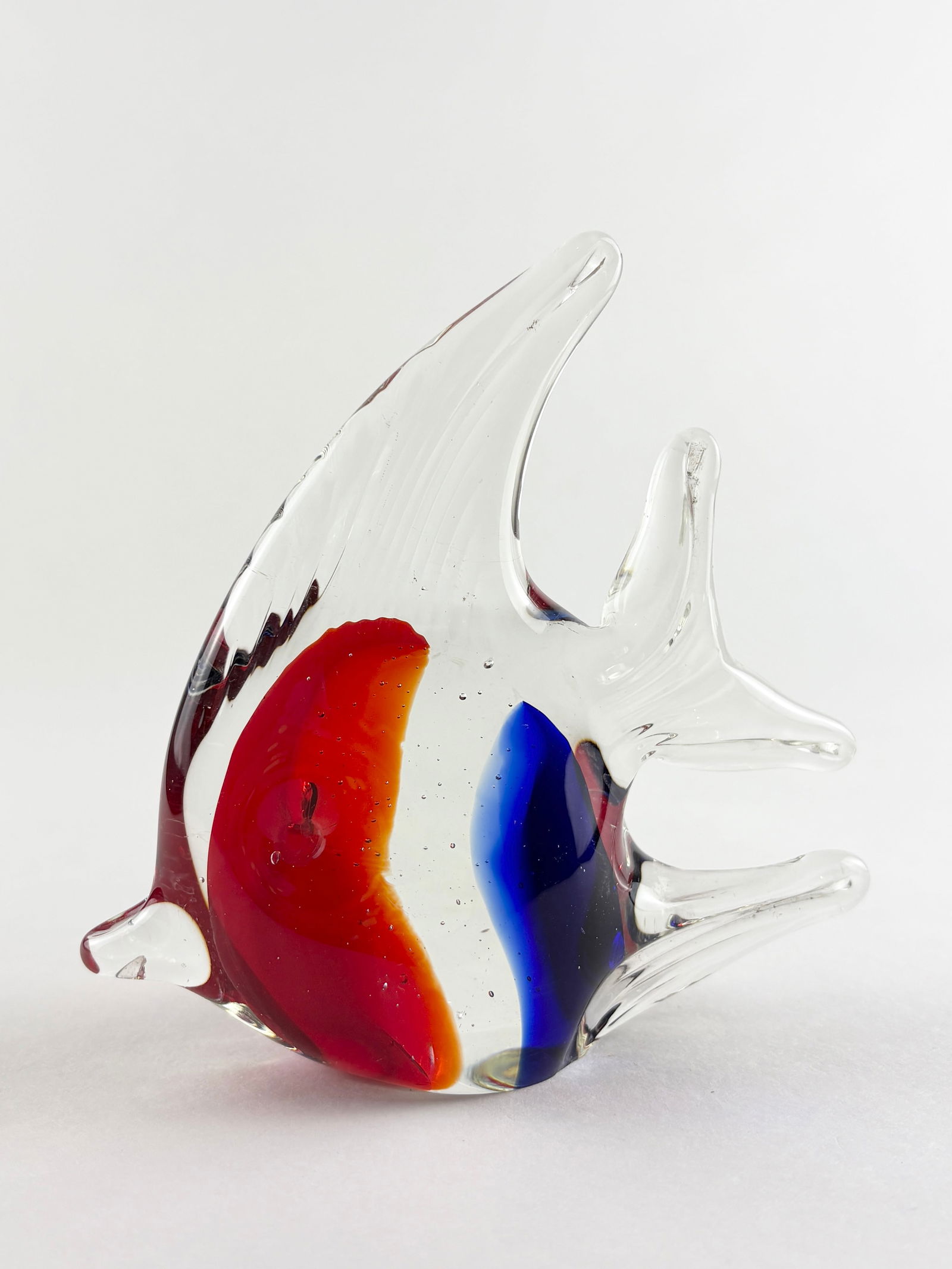 Glass Fish Sculpture (Murano Style): Decorative art glass fish sculpture featuring a clear body with bold encased red, blue, and amber coloration forming a central core. The elongated dorsal fin and stylized fins are typical of Murano-st