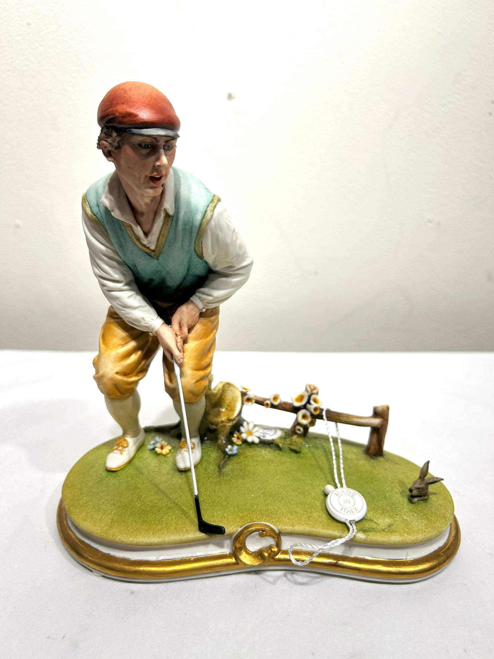 Capodimonte Porcelain Figurine: Golfer Preparing to Swing: This detailed Capodimonte porcelain figurine captures a golfer in the moment before taking a swing. The figure is dressed in golfing attire, including a cap, vest, and knickers, and is posed with a go