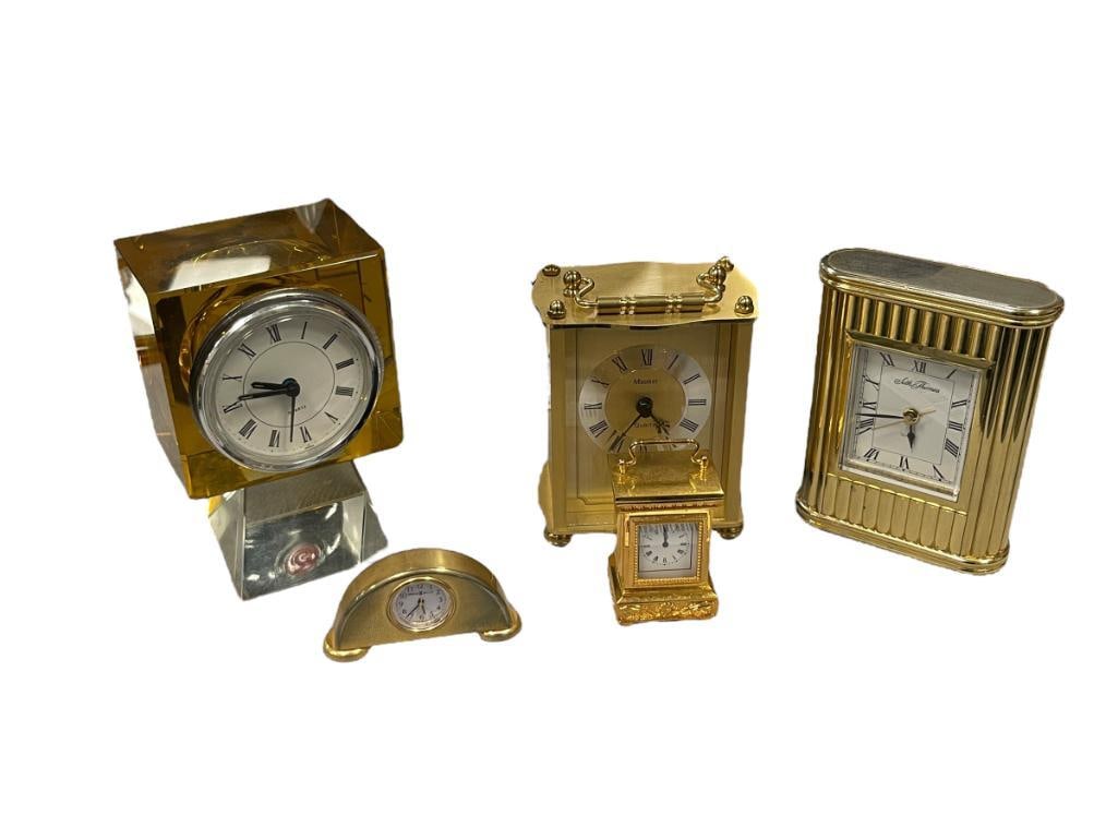 FIVE POLISHED BRASS FINISH DESK / TABLE CLOCKS PLUS CUT GLASS CLOCK: INCLUDES HOWARD MILLER MANTLE CLOCK PAPERWEIGHT CLOCK, SETH THOMAS BATTERY OPERATED CLOCK, CUT GLASS AMBER AND CLEAR GLASS DESK CLOCK, ALL NEED NEW BATTERIES 2 7/8" UP TO 5 3/8"