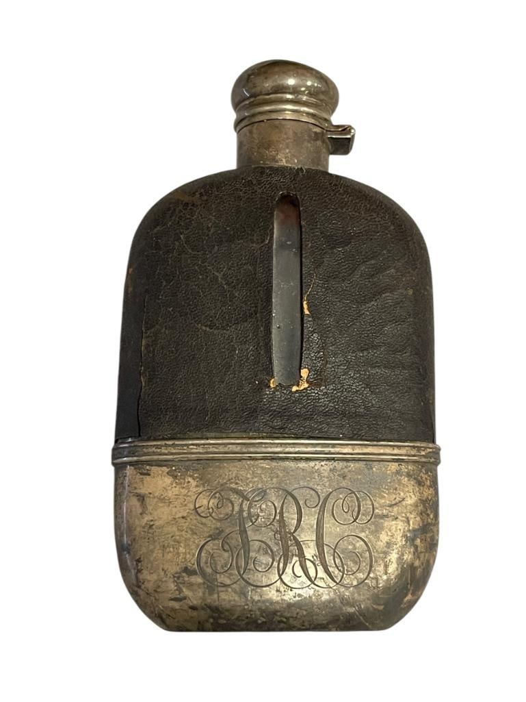 ANTIQUE STERLING SILVER AND GLASS 1/8 PINT FLASK WITH LEATHER WRAPPED TOP HALLMARKED: GLASS 1/8 PINT FLASK WITH LEATHER WRAPPED TOP, STERLING SILVER WRAPPED BOTTOM WITH MONOGRAM, STERLING SILVER HINGED TOP, HALLMARKED, LEATHER SHOWS WEAR 5 7/8" H