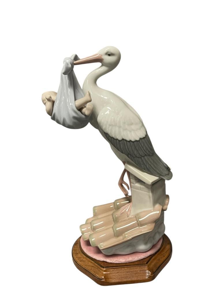 1994 LLADRO PORCELAIN FIGURINE SPECIAL GIFT # 6228 RETIRED IN 2001: LLADRO FINE PORCELAIN FIGURINE, SPECIAL GIFT, RETIRED IN 2001, DEPICTS HERON HOLDING BABY WITH BEAK WRAPPED IN A BLANKET, INCLUDES WOODEN BASE WITH CLOTH WRAPPED TOP, MADE IN SPAIN 9 3/4" H