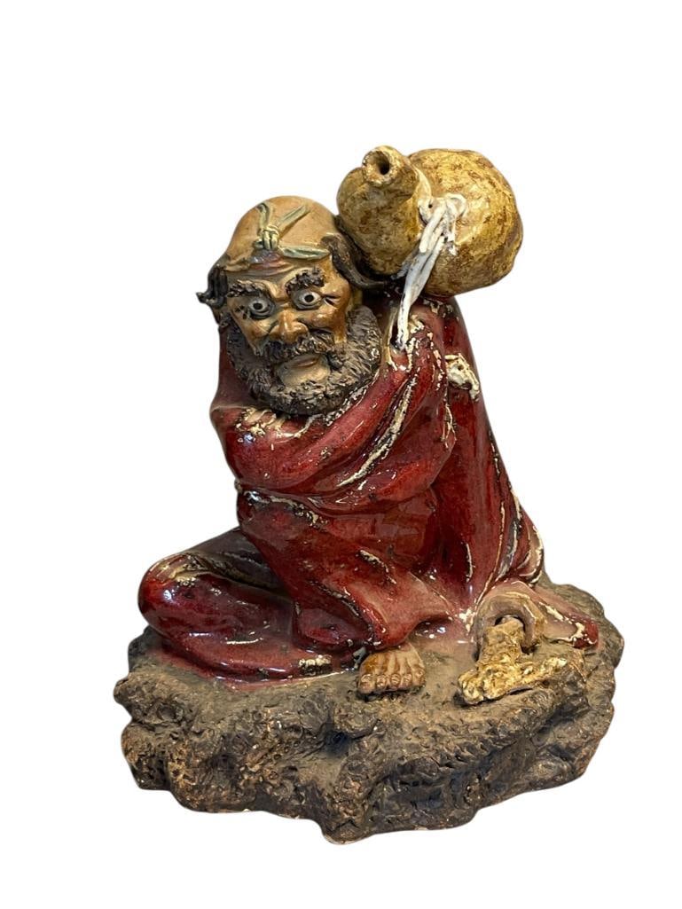 CHINESE SHIWAN POTTERY FIGURE SHIWAN KILNS GUANGDONG PROVINCE, CHINA FLAMBE OXBLOOD GLAZE: SHIWAN POTTERY FIGURE OF A SEATED ELDER MAN HOLDING STAFF AND GOURD ON HIS BACK IN FLAMBE OXBLOOD GLAZE, HANDS, FEET, AND HEAD ARE SHOWN IN NATURAL CLAY 11 7/8" H