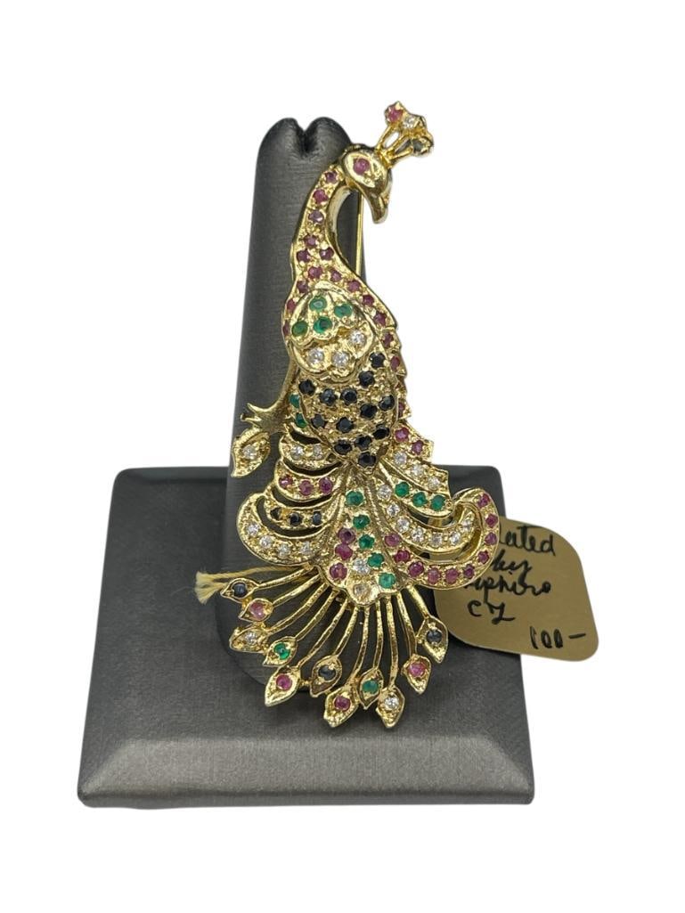 GOLD PLATED SAPPHIRE AND RUBY FIGURAL PEACOCK BROOCH: BROOCH IS ACCENTED WITH BLUE SAPPHIRE, RUBIES, SIMULATED GREEN EMERALDS, AND CUBIC ZIRCONIA 2 3/4", 2MM SAPPHIRES AND RUBIES