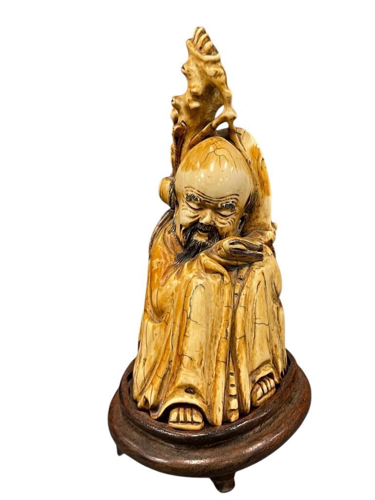EARLY 19TH CENTURY HAND CARVED BONE CHINESE FIGURE OF POSSIBLY SHOU-LAO GOD OF LONGEVITY: CARVED FROM A SINGLE PIECE OF BONE, SHOWS GOOD DETAIL, DISCOLORING FROM AGE, STAMPED ON THE BOTTOM, PRICE TAG FOR $458, ITEM SHOWS AGE, NO DAMAGE OR REPAIRS, CARVED WOOD BASE INCLUDED 6 3/4" H W/O BAS