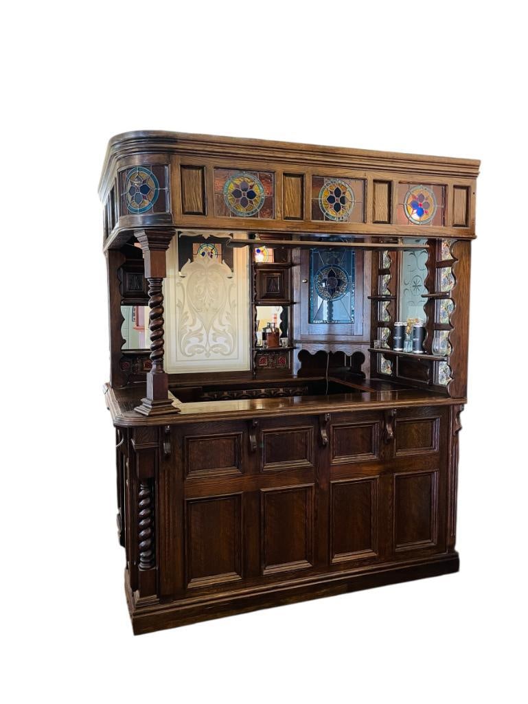 ANTIQUE IRISH PUB BAR FEATURING STAINED GLASS, ETCHED GLASS, AND DARK STAINED OAK: WRAP AROUND DESIGN, BOWED STAINED GLASS, FROSTED GLASS BACK DROP, HAND PAINTED TILE INSERTS, ONE GLASS IS CRACKED, SLIGHT CRACK FINISH, OVERALL GOOD CONDITION, VIEWABLE BY APPOINTMENT SATURDAY ONLY, M