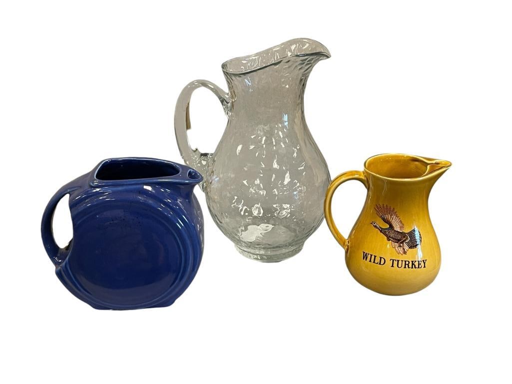 CERAMIC AND GLASS PITCHERS FIESTA DISC PITCHER, WILD TURKEY WHISKEY PITCHER, GLASS PITCHER: COBALT BLUE FIESTA PITCHER, WILD TURKEY ADVERTISEMENT WHISKEY PITCHER, FIESTA PITCHER HAS CRACK IN THE GLAZE NEAR RIM 6", 6 1/4", AND 10 1/4" H 