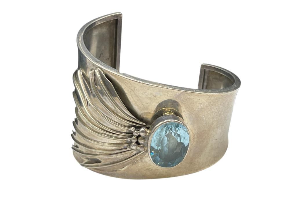 VINTAGE DESIGNER SIGNED STERLING SILVER WINGED TOPAZ BANGLE BRACELET: FEATURING AN OVAL CUT BLUE TOPAZ WITH WINGED TAIL 2 1/2" CUFF WIDTH, 2 1/4" AT WIDEST, 69.08 GRAMS