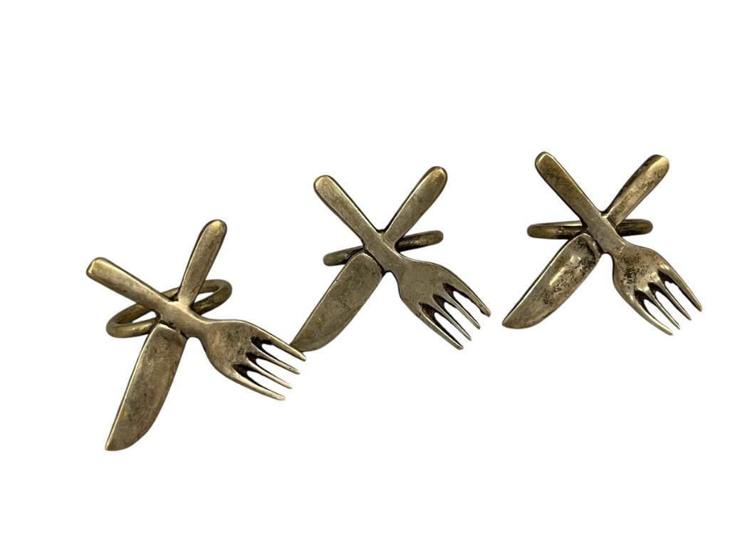 VINTAGE BRASS PLATED CROSSED FORK AND SPOON NAPKIN RINGS CIRCA 1960'S - 1970'S: FINISH SHOWS WEAR / PATINA, SET OF THREE 2" H 