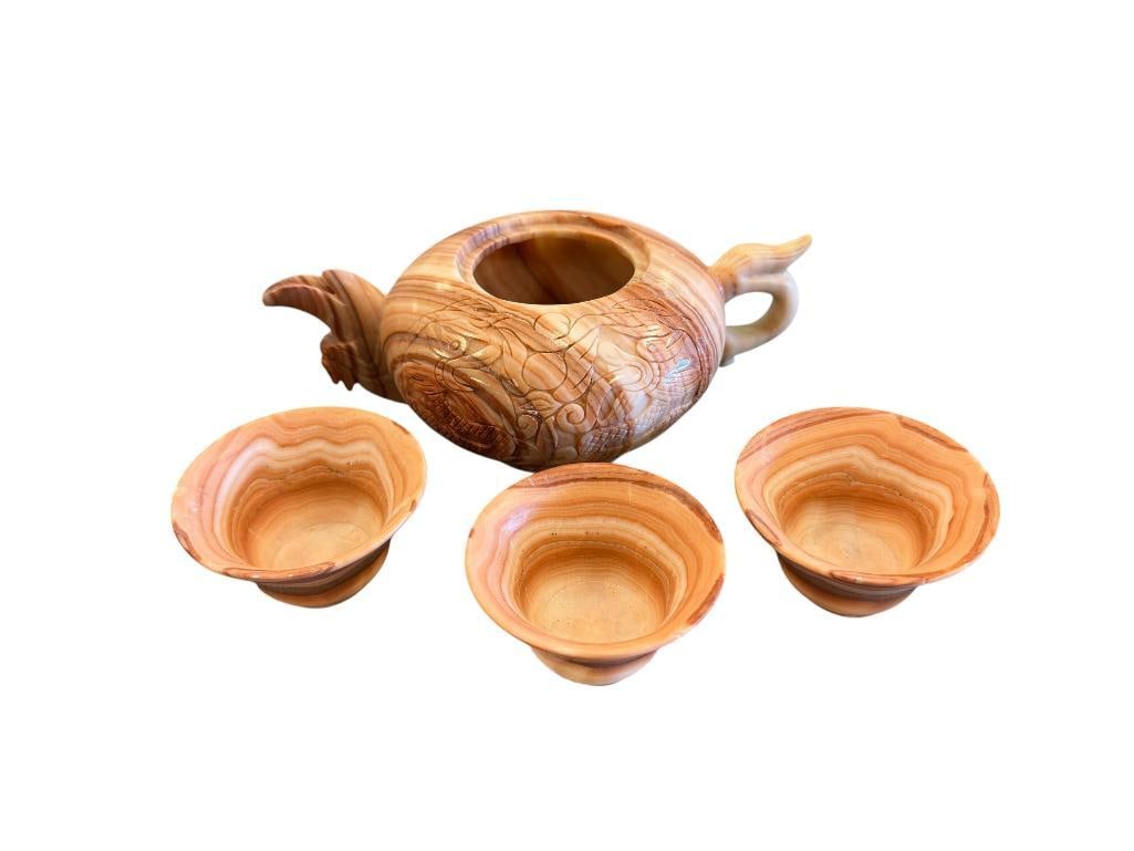 VINTAGE ALABASTER CARVED TEA SET FEATURING DRAGON FLOWER DESIGN ON TEAPOT WITH THREE TEACUPS: FEATURING BURNT ORANGE AND PEACH HUES, MINOR STRESS CRACKS AND TEACUPS, NO LID ON TEAPOT 8" X 3" TEAPOT, 3" X 1 3/4" TEACUPS 