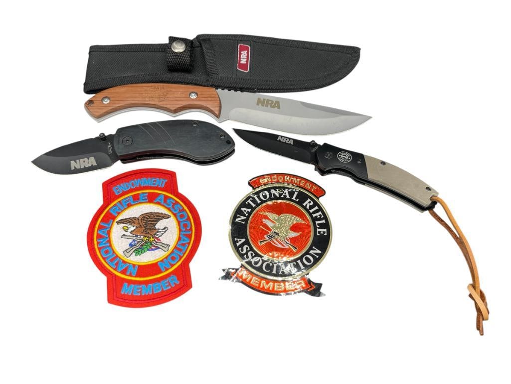 ASSORTED NRA COLLECTIBLE KNIVES, PATCH, AND STICKER: INCLUDES NRA FULL TANG CLIP-POINT BLADE WITH WOODEN HANDLE AND NYLON BELT CASE, AND TWO NRA STONE RIVER BLACK STAINLESS STEEL FOLDING KNIVES LARGEST BLADE IS 5", 9 1/4" TOTAL LENGTH 