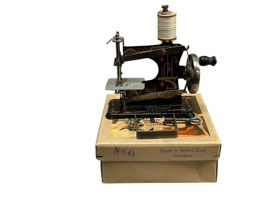 VINTAGE CASIGE SEW-O-MATIC CHILDRENS TOY SEWING MACHINE CIRCA 1900'S - 1930'S: STAMPED METAL BODY WITH RED AND GOLD GEOMETRIC DESIGN, MADE IN BRITISH-ZONE GERMANY, FINISH ON BASE SHOWS WEAR, OVERALL IN GOOD CONDITION FOR ITS AGE, INCLUDES ORIGINAL BOX WITH ILLUSTRATION, AND CLAM