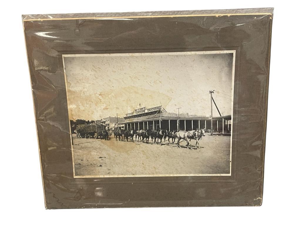 CIRCA 1908 PHOTOGRAPH OF A COACH PULLING 18 CORDS OF WOOD BY 13 HORSES FALLON,NV: PHOTOGRAPH SHOWS 18 CORDS OF WOOD BEING PULLED BY 13 HORSE IN FRONT OF THE I.H. KENT GENERAL STORE, INFORMATION ON THE BACK, SOME WATER DAMAGE 14" X 12"