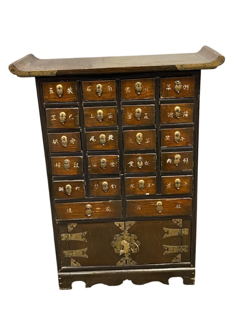 20TH CENTURY KOREAN APOTHECARY / MEDICINE CABINET: HAND CRAFTED CABINET WITH 22 DESIGNATED DRAWERS, EACH WITH WRITING ON THE FRONT OF THE DRAWER, BOTTOM STORAGE, FEATURES BRASS OVERLAY HARDWARE, LIGHT WEAR ON THE TOP 20" X 8 1/2" X 26 1/4" H