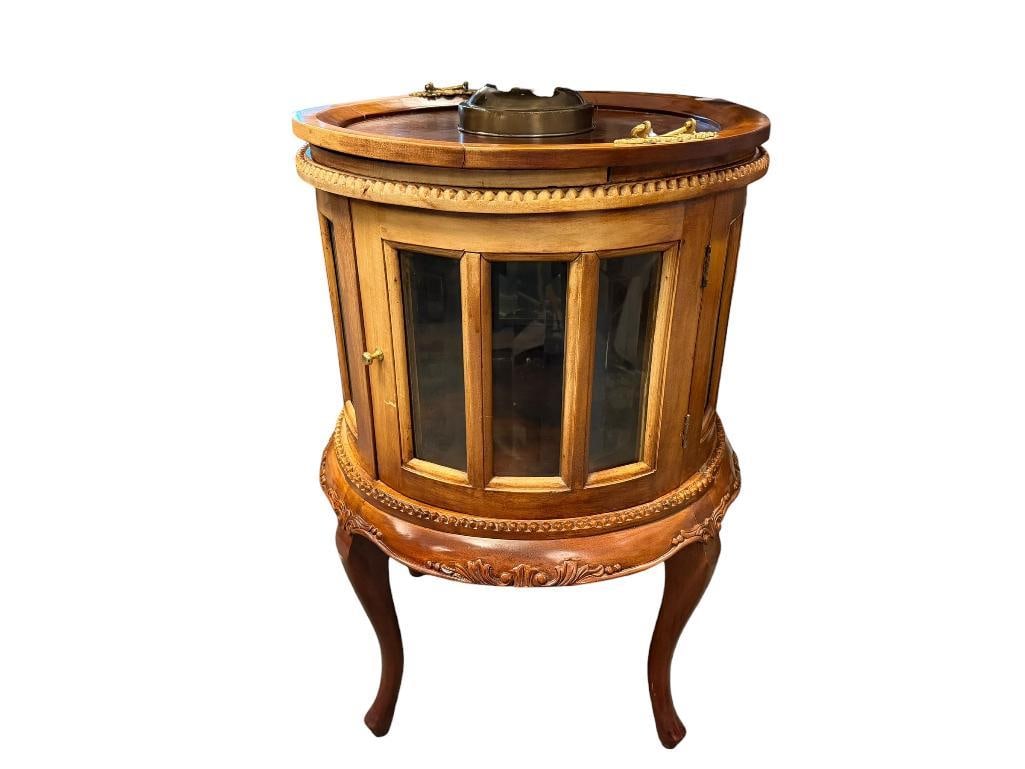 FOUR-LEGGED ROUND DISPLAY TABLE WITH SERVING TRAY: FEATURES 12 BEVELED GLASS PANELS WITH SWING DOOR, REMOVABLE TRAY WITH BRASS HANDLES, DECORATIVE CARVED SKIRT, BOTTOM OF TABLE HAS SPLIT, ALSO FINSH SHOWS FADING / SUN DAMAGE 19 1/2" ROUND, 30" H
