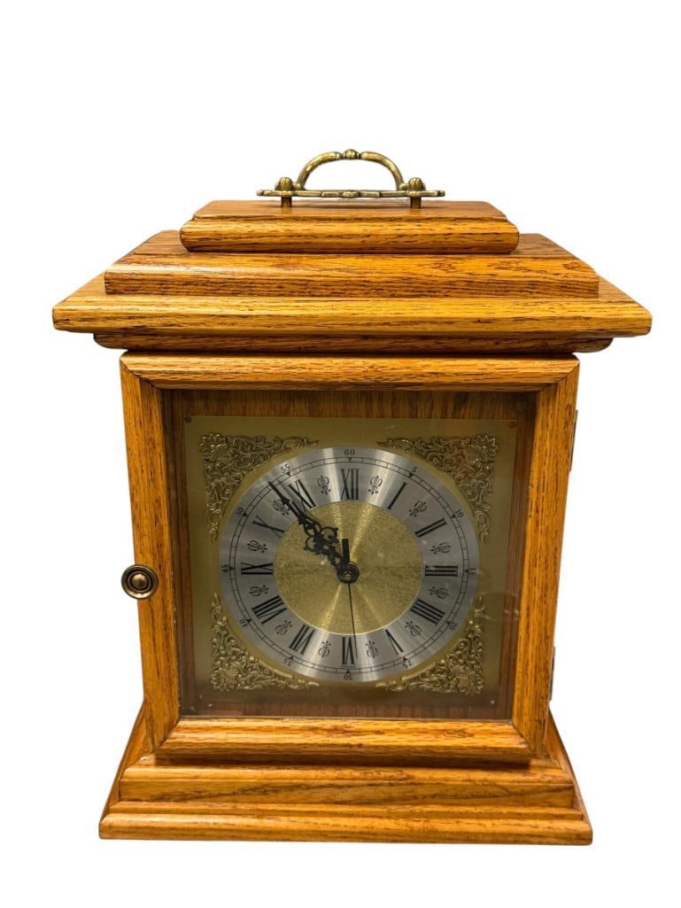 HAND CRAFTED SOLID OAK MANTLE CLOCK BATTERY OPERATED: BRASS AND BRUSHED SILVER FINISH ROMAN NUMERAL DIAL, FEATURES GLASS FRONT DOOR WITH BRASS HANDLE 12 1/2" X 6" X 15 1/2" H
