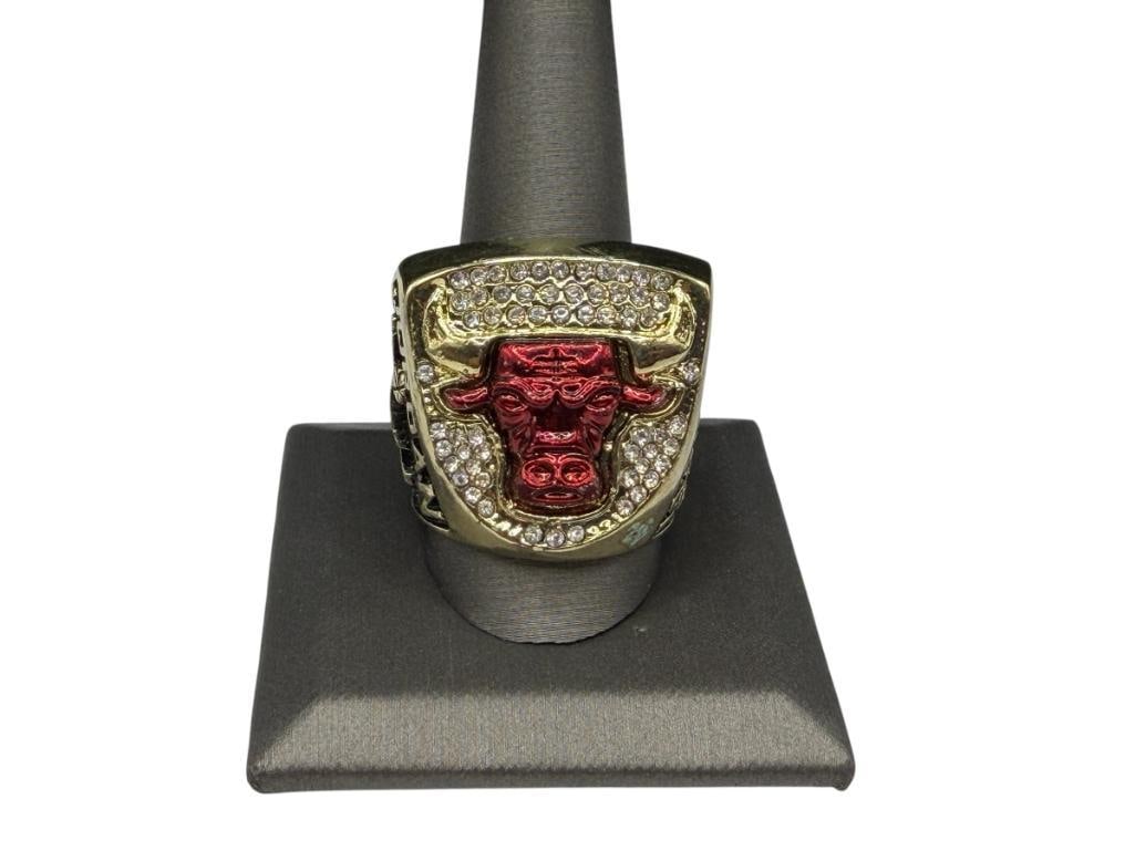 1993 CHICAGO BULLS MICHAEL JORDAN NBA CHAMPIONSHIP REPLICA RING: "3-PEAT," RED ENAMELED BULLS LOGO WITH CLEAR STONE ACCENTS, GOLD TONE STAINLESS STEEL RING SIZE 12, 1" FRONT