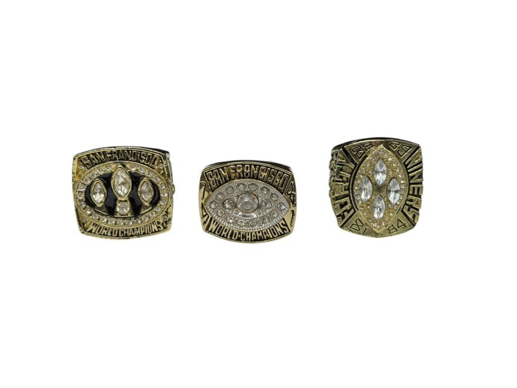 THREE SAN FRANCISCO 49ERS SUPER BOWL REPLICA RINGS INCLUDING JOE MONTANA AND JERRY RICE: ALL GOLD TONE STAINLESS STEEL AND ACCENTED WITH CLEAR STONES, INCLUDES TWO JOE MONTANA RINGS AND ONE JERRY RICE RING, 1982, 1988, AND 1989, FEATURING INFO FROM SEASON AND MORE DETAILS SIZE 11, 12, AND