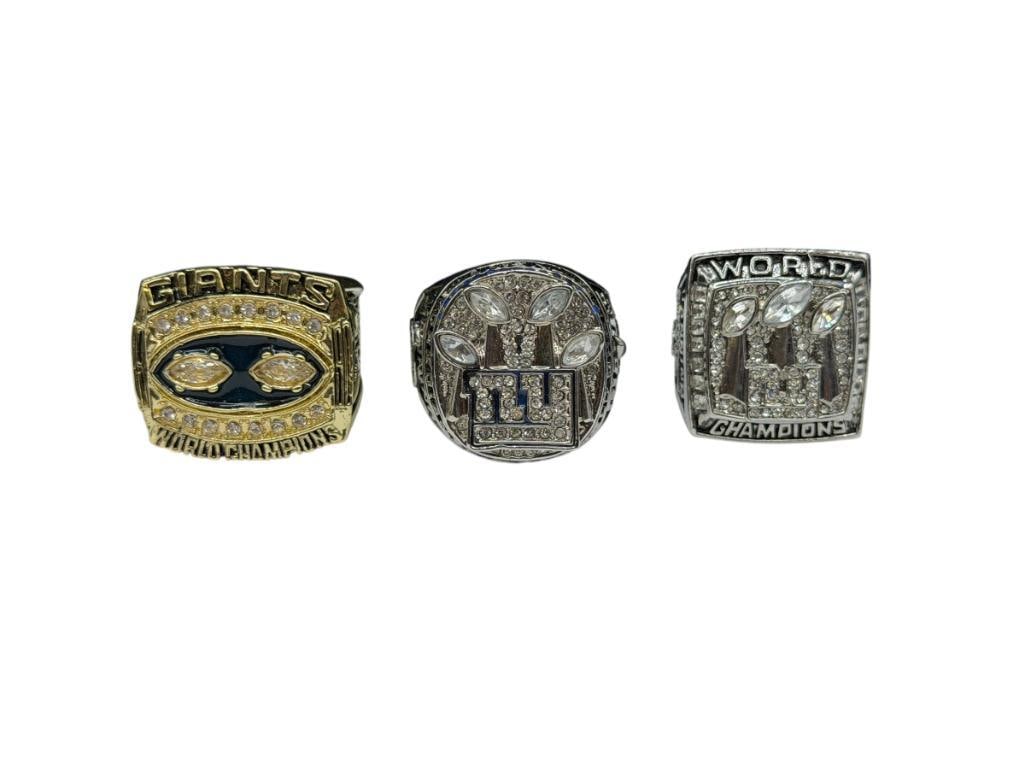 THREE NEW YORK GINATS NFL SUPER BOWL CHAMPIONSHIP REPLICA RINGS INCLUDING ELI MANNINGS AND L. TAY...: STAINLESS STEEL WITH CLEAR STONE ACCENTS AND ONE GOLD TONE DESIGN, TWO ELI MANNING AND ONE LAWRENCE TAYLOR, FEATURING VARIOUS DETAILS ON EACH RING SIZES 11 AND 13, UP TO 1 1/8" FRONTS