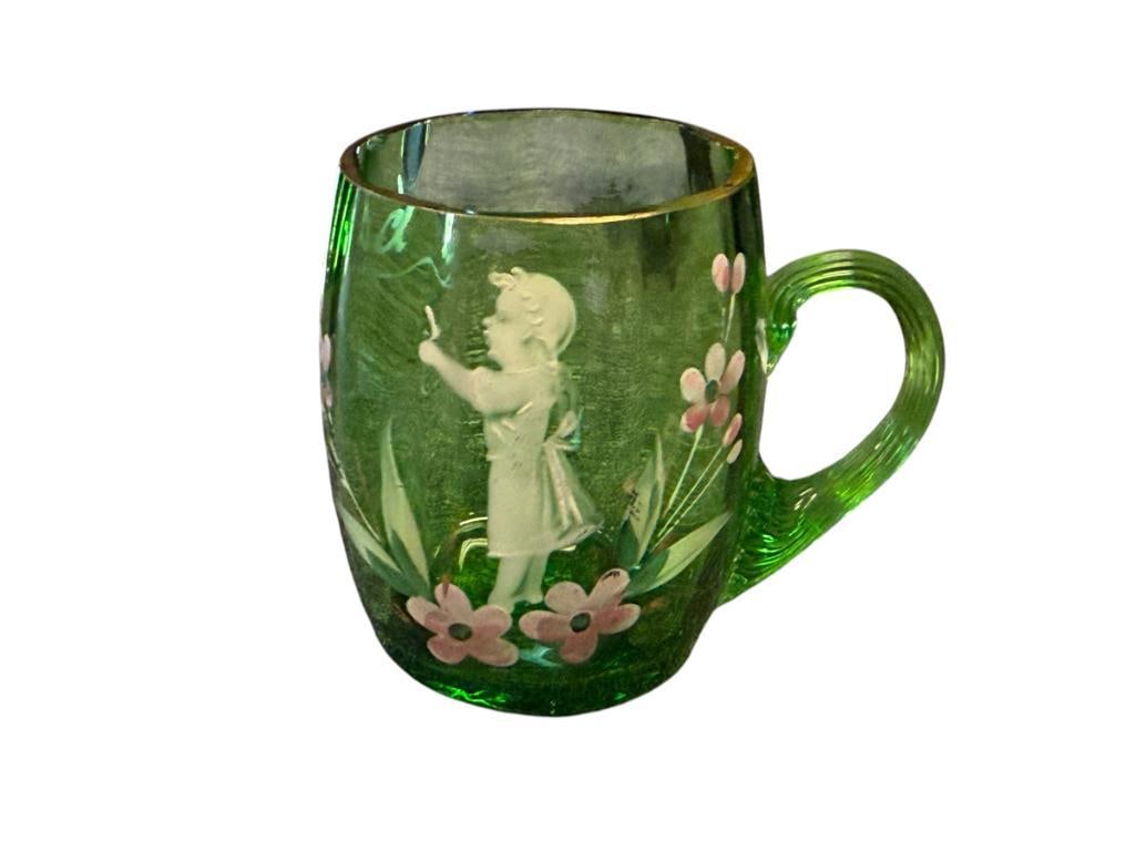 ANTIQUE HAND BLOWN ART GLASS EMERALD GREEN MARY GREGORY BABY CUP WITH GILT ACCENTS: HAND PAINTED BABY CUP WITH IMAGE OF A YOUNG GIRL AND FLOWERS, APPLIED HANDLE, DOES HAVE THREE "TINY" CHIPS ON THE INNER EDGE OF THE RIM 2 3/8" H