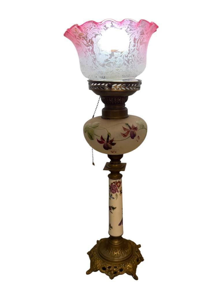ANTIQUE VICTORIAN STYLE PARLOR LAMP WITH ORNATE BRASS BASE AND FLORAL DESIGN: INCLUDES CLEAR TO CRANBERRY RUFFLE RIM SHADE, HAND PAINTED FROSTED GLASS FONT, AND FLORAL PORCELAIN COLUMN, TESTED + 22" H