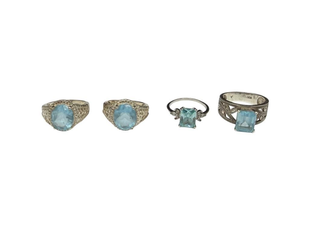 FOUR STERLING SILVER RINGS INCLUDING ONE WITH EMERALD CUT BLUE TOPAZ: OTHER THREE RINGS FEATURE SIMULATED TOPAZ STONES VARIOUS SIZES, 10MM X 8MM BLUE TOPAZ, 17.19 GRAMS TOTAL