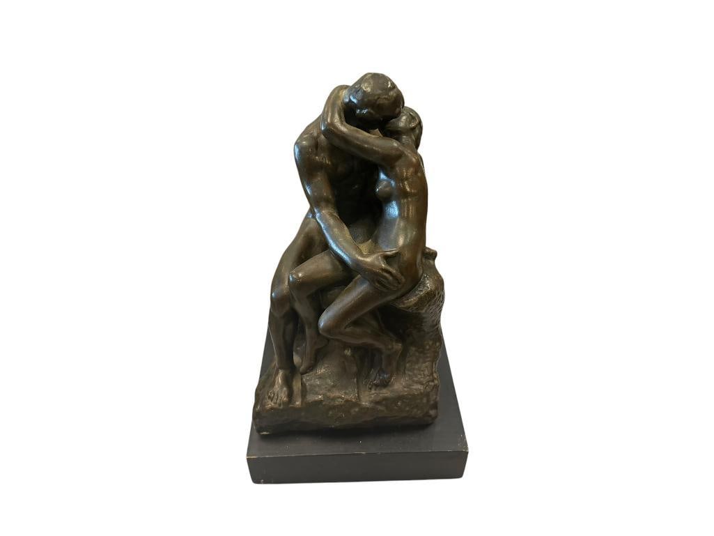 AUSTIN PRODUCTION THE KISS BY AUGUSTE RODIN ROMANTIC CERAMIC SCULPTURE: BRONZE TONED CERAMIC SCULPTURE OF A NUDE WOMAN AND MAN, MARKED ALONG THE BOTTOM EDGE, FEW CHIPS ALONG THE BOTTOM EDGE, WOODEN BASE INCLUDED FOR DISPLAY 12" H ON BASE