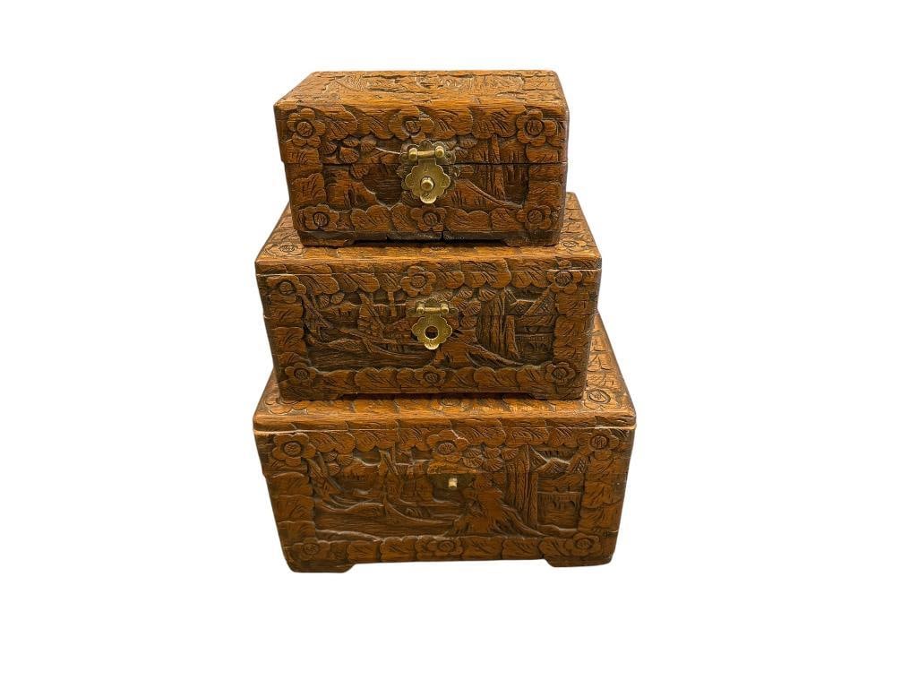 SET OF FOUR ANTIQUE CARVED CAMPHOR WOOD ASIAN NESTING BOXES FEATURING INTRICATE LANDSCAPE CARVINGS: EACH HAS BRASS CLOSURES, TWO CLOSURES ARE PARTIALLY DAMAGED LARGEST IS 12" X 7" X 7 1/2"