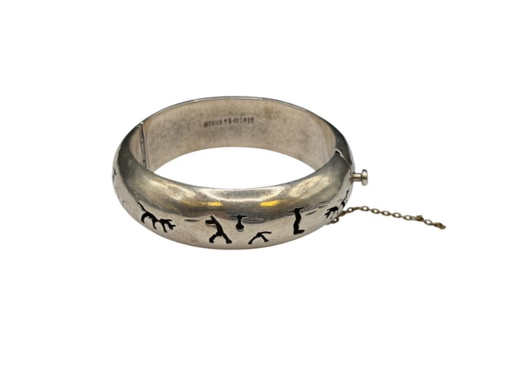 VINTAGE TAXCO MEXICO STERLING SILVER STORYTELLING PIERCED DESIGN BANGLE BRACELET: MARKED "MEXICO TS-120 P25", HINGED DESIGN, SAFETY CHAIN IS DAMAGED 2 1/2" BANGLE WRIST WIDTH X 13/16" THICK, 64.32 GRAMS