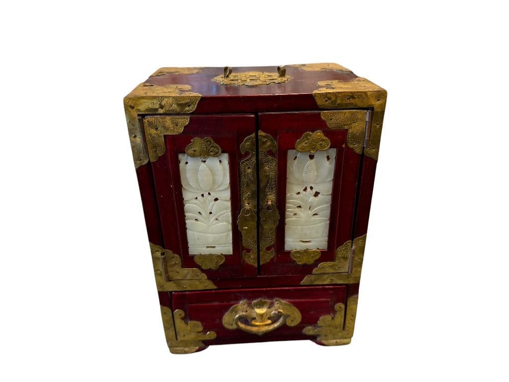 CHERRY FINISHED CHINESE JEWELRY CHEST WITH ELABORATE BRASS OVERLAY AND CARVED STONE ACCENT DOORS: PIERCED AND ENGRAVED BRASS OVERLAY WITH CARVED STONE INLAY DOORS, GOLD EMBROIDERED RED SILK INTERIOR, MISSING TOP HANDLE 6" X 4 1/2" X 8 /2"