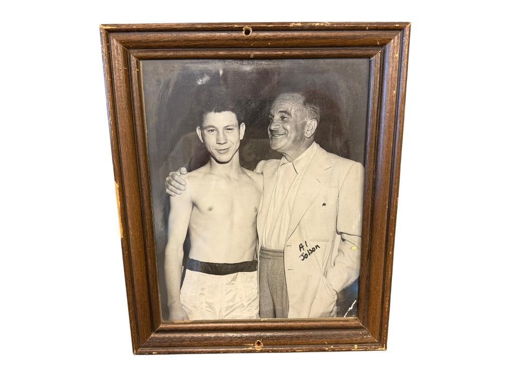 1940'S BLACK AND WHITE PROMOTIONAL PHOTOGRAPH OF AL JOLSON POSING WITH YOUNG BOXER: AL JOLSON WAS AN AMERICAN SINGER AND ACTOR IN THE EARLY 20TH CENTURY, SIGNED IN BLCK MARKER, FRAMED 9 1/2" X 11 1/2" FRAME