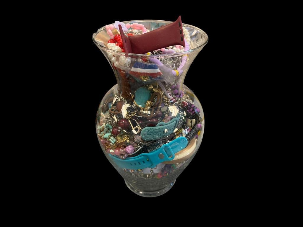 GLASS VASE FILLED WITH ASSORTED COSTUME JEWELRY FEATURING VARIOUS DESIGNS AND STYLES: INCLUDES GOLD TONE AND SILVER TONE PIECES, BEADED DESIGNS, NECKLACES, BRACELETS, APPLE WATCH BANDS, AND MORE JAR IS 10 3/4"