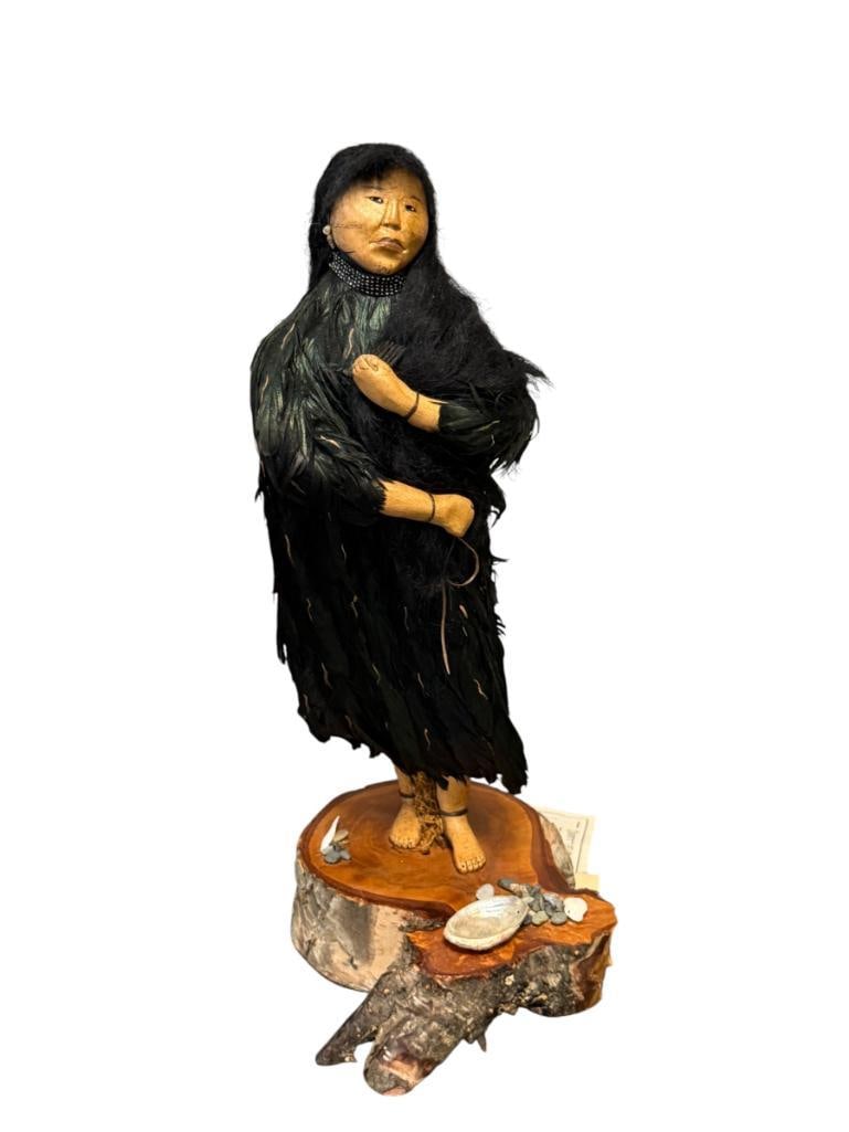 EARLY 21ST CENTURY HAND CRAFTED POTTERY ALEUT PEOPLE FIGURINE BY LINDA DURAN NO. 934: HAND CRAFTED POTTERY FIGURINE DECORATED WITH FEATHERS A SEA SHELLS, MOUNTED ON WOOD BASE, TITLED ALEUTHAN BEAUTY MADE IN 2003, SIGNED WITH ORIGINAL LABELS 13 1/2" H