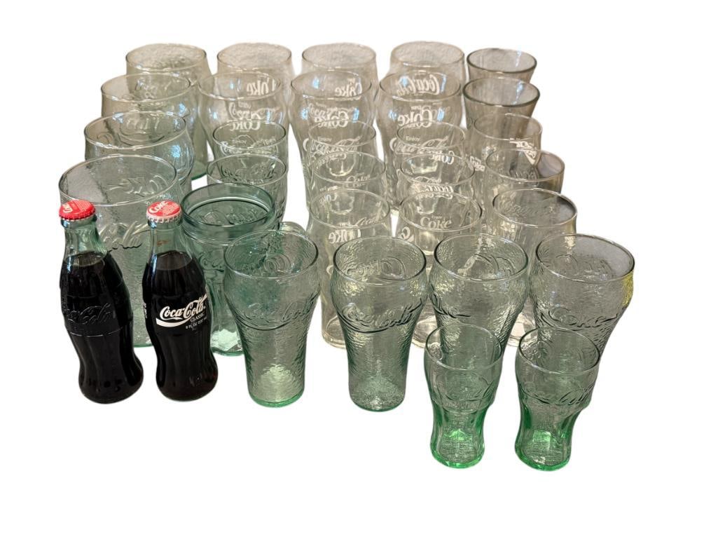 ASSORTMENT OF CLEAR AND AQUA COLORED GLASS COCA-COLA DRINKING GLASSES: CLEAR GLASSES HAVE WHITE LETTERING AND AQUA COLORED GLASS HAS EMBOSSED LETTERING AND DESIGN, VARIOUS STYLE GLASSES, TOTAL OF 30 AND TWO SEALED COCA-COLA BOTTLES 4 1/2" UP TO 7" GLASSES
