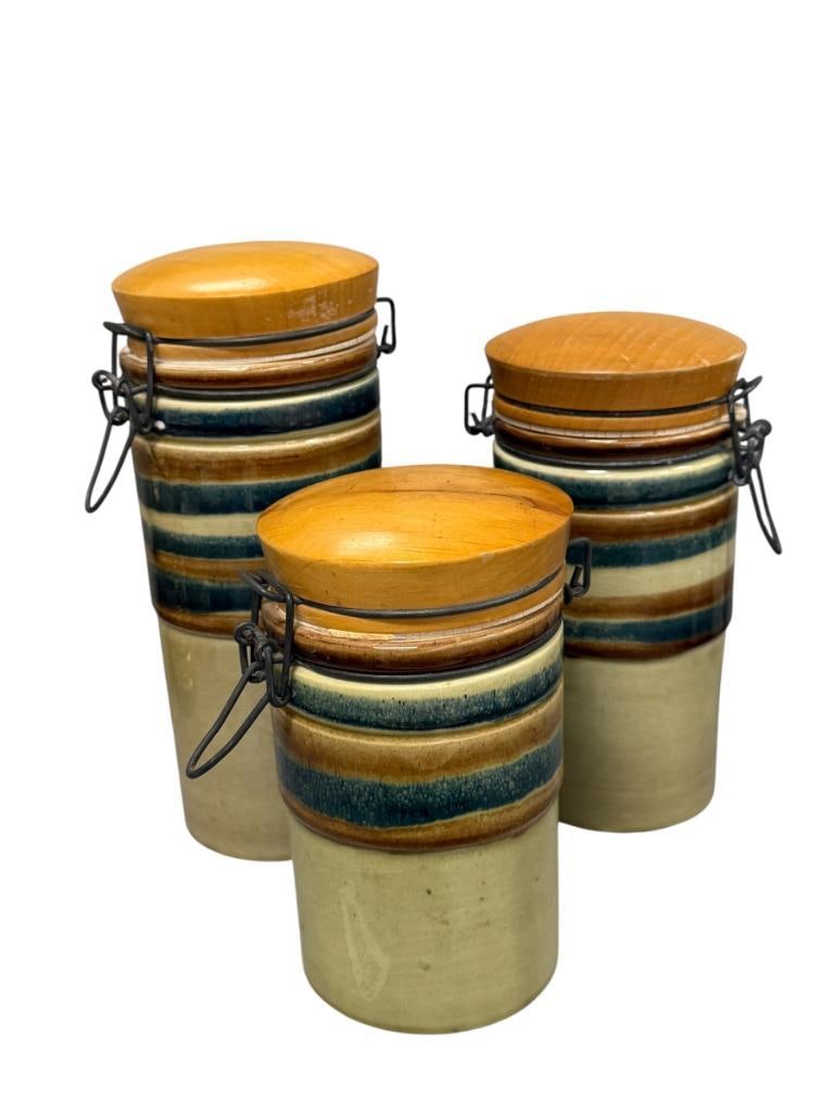 MID-CENTURY CERAMICHI BALDELLI POTTERY CANISTER SET MADE IN CITTA DI CASTELLO, ITALY: SET OF THREE IN BROWN GLAZE WITH EARTH TONED BANDS AND WOODEN LIDS, MARKED ON THE BOTTOM, LIGHT WEAR ON THE LIDS, RUBBER SEALS ARE CRACKED 6 1/2", 8", AND 9 1/4" H