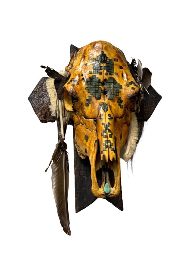 AMERICAN FOLK ART DECORATED STEER SKULL WITH TURQUOISE, FEATHERS, GEOMETRIC PAINTED DESIGN: PAINTED STEER SKULL IN RUSTIC BURNED FINISH DECORATED WITH TURQUOISE ON THE SNOUT AREA, ALSO DECORATED WITH FEATHERS AND BEADWORK, MOUNTED ON STYLIZED CROSS PLAQUE FOR DISPLAY 17" X 21" OVERALL
