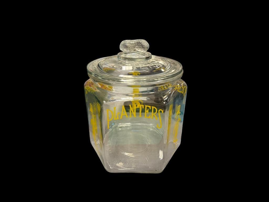 VINTAGE PLANTERS PEANUTS GLASS STORE COUNTER TOP JAR WITH YELLOW LETTERING AND ILLUSTRATIONS: CIRCA 1930'S, HEXAGONAL SHAPE, LID HAS DAMAGE ON THE BOTTOM, HAS BEEN SANDED DOWN, JAR HAS NO CHIPS OR CRACKS 9 1/2" H