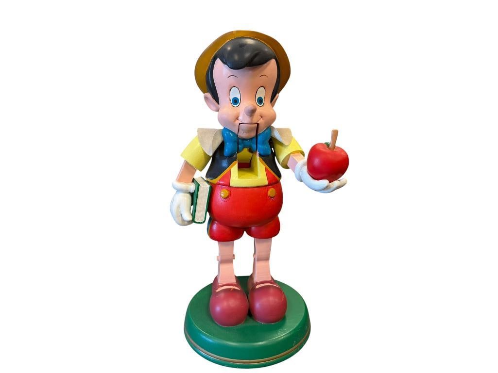 WALT DISNEY CO. HEAVY PAINTED WOOD PINOCCHIO NUTCRACKER: PINOCCHIO HOLDING APPLE NUTCRACKER STANDING ON ROUND BASE, MARKED ON THE BOTTOM, LIGHT SCUFFS AROUND THE BASE 12 1/2" H