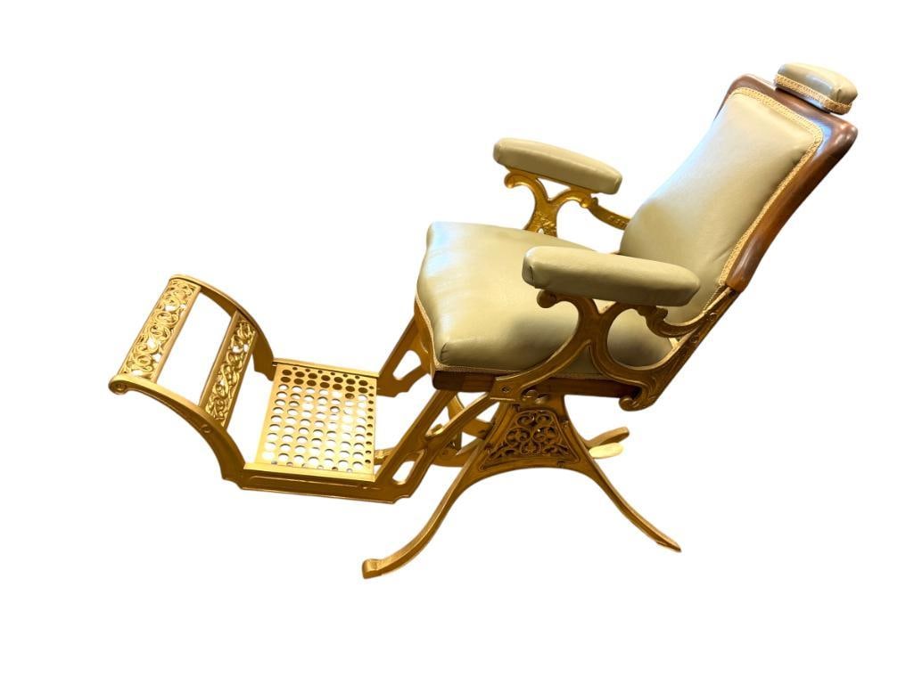 ANTIQUE RESTORED BARBER CHAIR: FEATURES GOLD FINISH CAST IRON FRAME, ADJUSTABLE TILT, WALNUT TRIM ALONG THE SEAT AND BACK REST, ADJUSTABLE NECK REST, FAUX LEATHER UPHOLSTERY WITH TRIM 48" X 24" X 44"