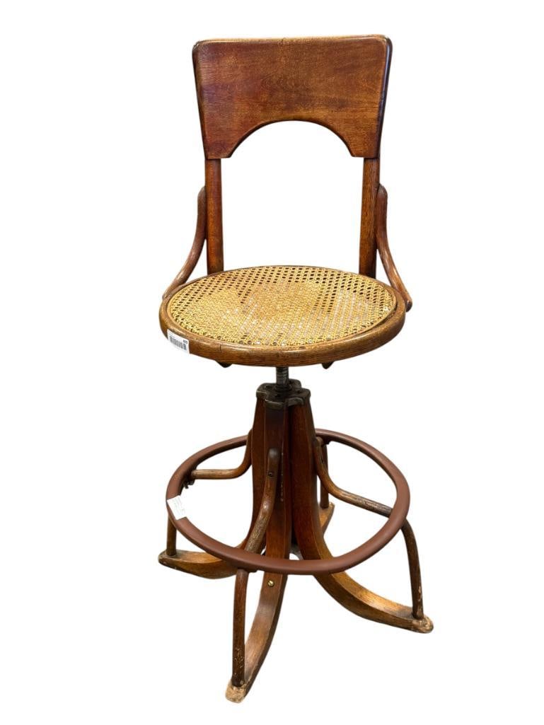 ANTIQUE BENTWOOD SCREW HEIGHT ADJUSTABLE STOOL WITH CANE SEAT: FEATURES SCREW HEIGHT ADJUSTABLE SEAT, ROUND FOOT REST, CANE SEAT SHOWS WEAR, FEET OF THE STOOL SHOW WEAR FROM POSSIBLE DOG CHEWING 