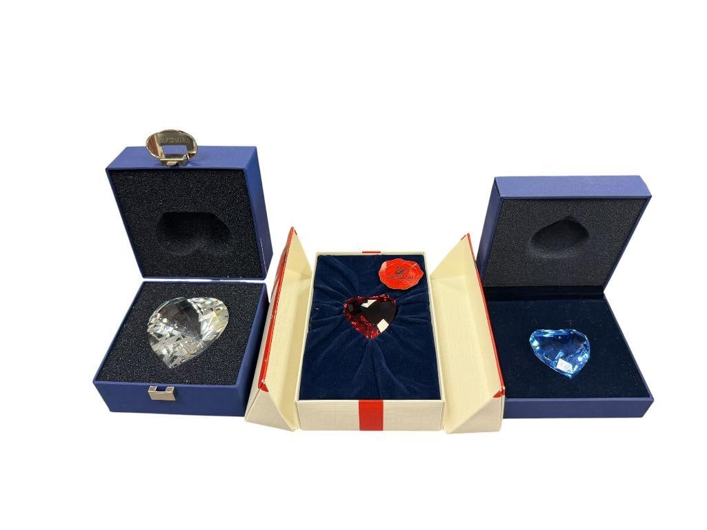 SWAROVSKI CRYSTAL TRIO OF HEARTS IN RUBY RED, COBALT BLUE AND CLEAR CRYSTAL: EACH HEART FEATURES THE SWAN LOGO MARK, EACH IS IN MINT CONDITION WITH ITS ORIGINAL BOX, NO CHIPS OR REPAIRS 1 1/2", 1 5/8", AND 2 3/8"