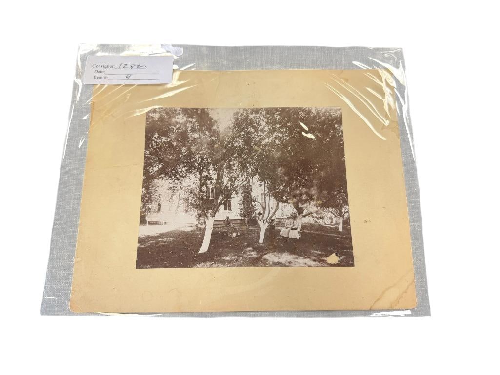 EARLY 1900'S SEPIA TONED PHOTOGRAPH OF ORMSBY HOUSE IN CARSON CITY, NV: ORMSBY HOUSE WAS A WOMAN'S SHELTER / ORGANIZATION IN CARSON CITY, MARKED ON THE BACK IN PENCIL, PHOTO DEPICTS WOMEN SITTING IN A GRASSY AREA COVERED WITH TREES 9" X 7"