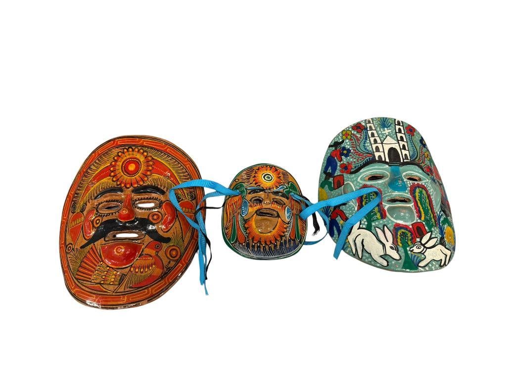 THREE HAND CRAFTED TERRACOTTA MEXICAN FOLK ART WALL MASKS: FEATURING WHIMSICAL HAND PAINTED MOTIFS WITH RABBITS, CHURCH, BIRD, FLOWERS, ETC., MASK WITH RABBITS AND CHURCH IS WRITTEN ON THE BACK, WAS PRESENTED AS A GIFT, ORANGE THEME MASK HAS A SMALL CHIP ON