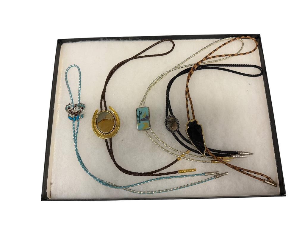 FIVE WESTERN THEMED BOLO TIES INCLUDES KNAPPED OBSIDIAN BOLO AND TWO POLISHED STONE BOLOS: ALSO INCLUDES BEJEWELED PHOENIX AND DESERT / CACTUS BOLO, EACH WITH BRAIDED TIES 1 1/4" UP TO 2 1/4" 