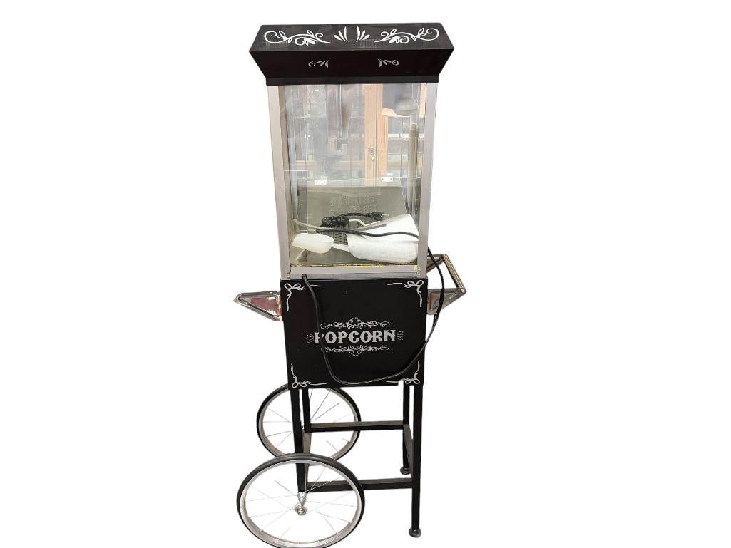 GREAT NORTHEN POPCORN COMPANY NOSTALGIC POPCORN MACHINE MODEL 83-DT5630: BLACK AND SILVER POPCORN MACHINE WITH CHROME WIRE WHEELS AND GRAB HANDLE, MISSING SIDE GLASS PIECE, AND ONE PIN FOR ONE OF THE HINGES 60" H