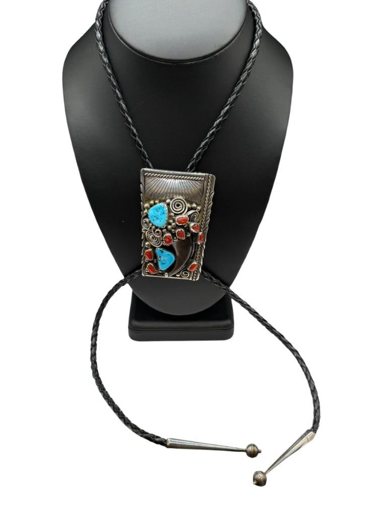 NAVAJO ARTIST SIGNED "EB" POSSIBLY EDISON BEGAY STERLING BEAR CLAW BOLO TIE WITH TURQUOISE AND CO...: FEATURING ELABORATE TOOLED SILVER DESIGN WITH SWIRLS ACCENTED A BEAR CLAW ALONGSIDE TURQUOISE AND CORAL, SIGNED BY ARTIST "EB", BLACK LEATHER BOLO WITH STERLING SILVER TIPS 3" CLIP, 1 1/4" CLAW,