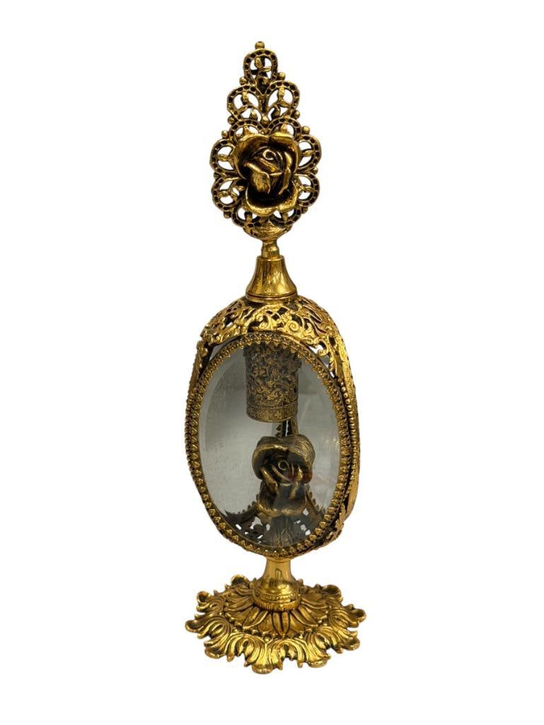 STYLEBUILT ACCESSORIES N.Y. GOLD ORMULU FILIGREE METAL FRANGRANCE / PERFUME BOTTLE WITH ROSE DESIGN: INTRICATE LEAF BASE WITH THREE WINDOW CENTER SHOWING ROSE AND GLASS ENCASED BOTTLE, LARGE ROSE HANDLED GLASS DAUBER, DAUBER AND BOTTLE ARE INTACT, MARKED ON THE BOTTOM 10" H
