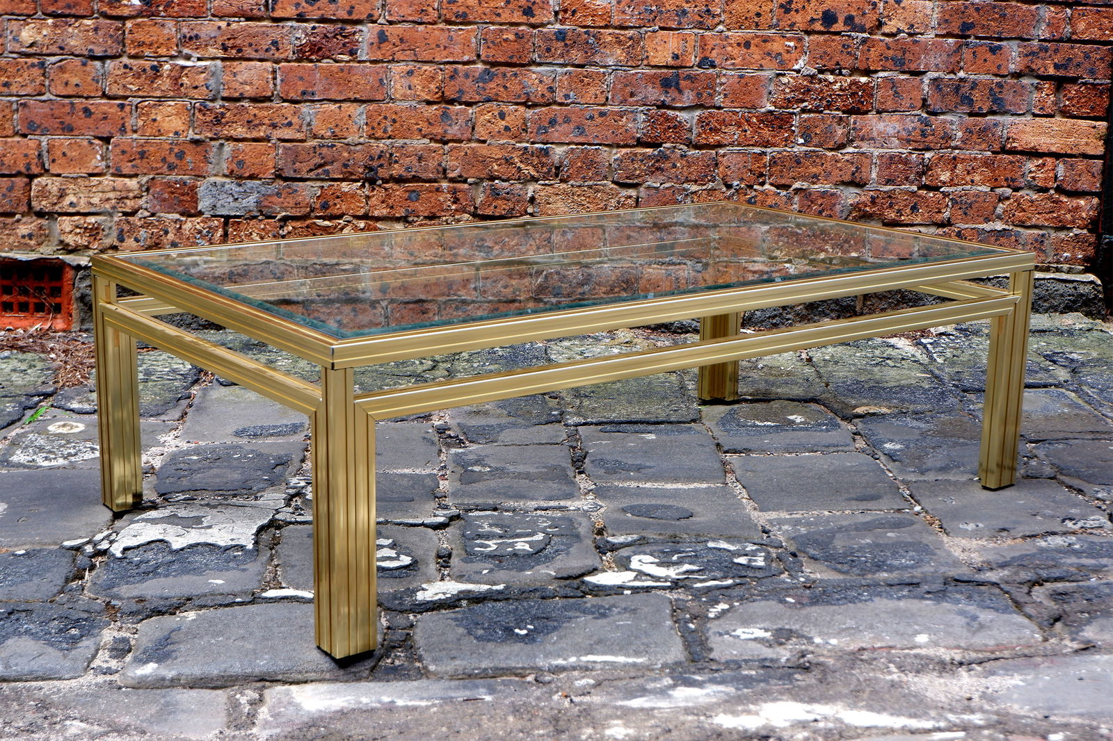 A gilt metal and glass coffee table by Pierre Vandel,: A gilt metal and glass coffee table by Pierre Vandel, with bevelled glass, the frame stamped: PIERRE VANDAL - PARIS, 38cm high, 175cm wide, 72cm deep