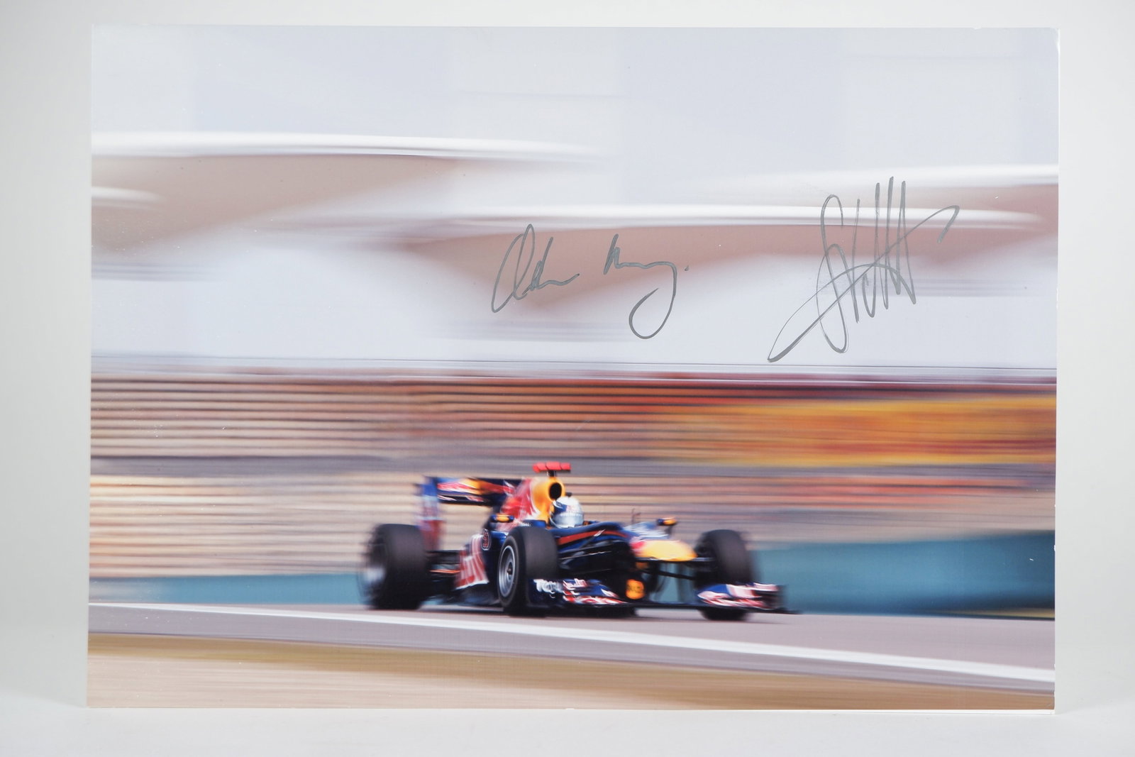 VETTEL/NEWEY: An image of S.Vettel racing a Red Bull F1. Image signed by S.Vettel & Adrian Newey: VETTEL/NEWEY: A colour image of Sebastian Vettel racing a Red Bull F1, image signed by Sebastian and Adrian Newey in silver marker; on photographic paper image measures approximately 29.5cm wide, 21cm