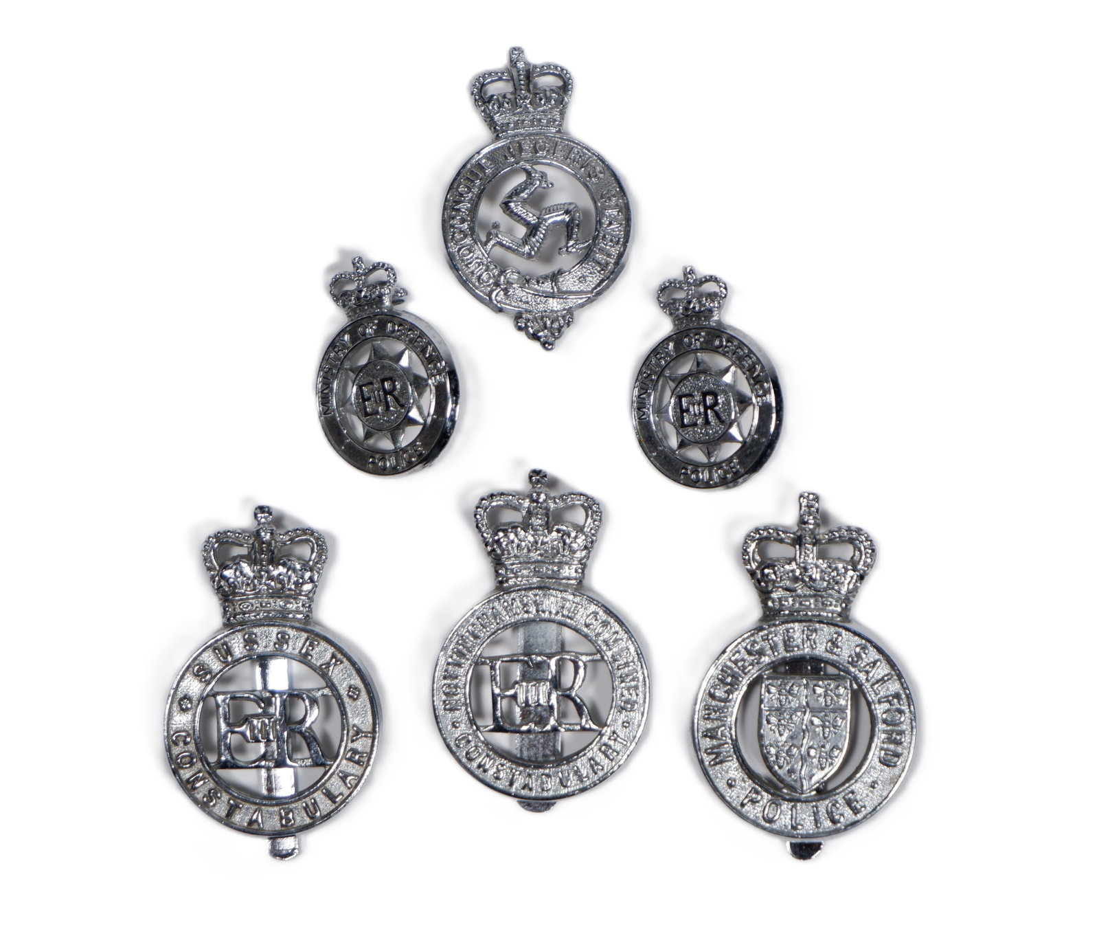 A collection of white metal cap badges: A collection of white metal cap badges, including An Isle of Man volunteers, Sussex police, Mancester and Salford police and Nottinghamshire Combined Constabulary