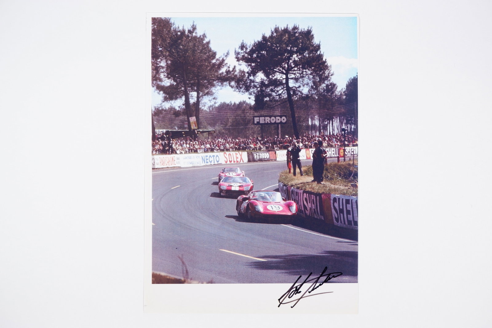 SURTEES: A colour image of John Surtees racing a Ferrari 330 P. Surtees signature: SURTEES: A colour image of John Surtees racing a Ferrari 330 P, image signed by Surtees in black; on thick stock paper, image measures approximately 21cm wide, 29.5cm high overall.